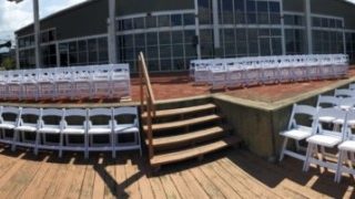 Outdoor venue with rows of white chairs.