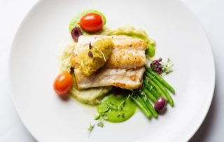 Gourmet fish dish with vegetables and garnish.