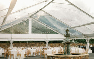 Clear tented wedding reception with large fountain in the middle and white tables with brown chairs